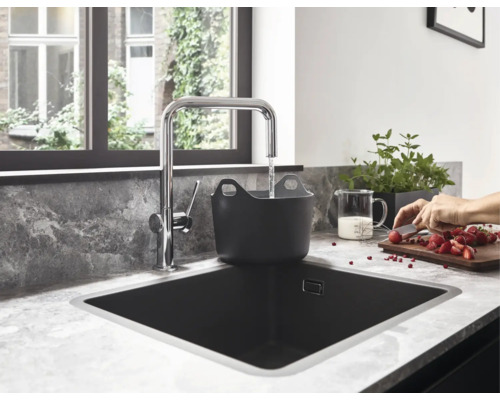 Cuisine moderne avec un robinet chromé en forme de L versant de l'eau dans un bac noir dans un évier noir sur un plan de travail marbré.