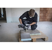 Handwerker bohrt mit einem Metabo Winkelschleifer und einer Diamantbohrkrone ein Loch in eine Steinplatte auf einer Baustelle.