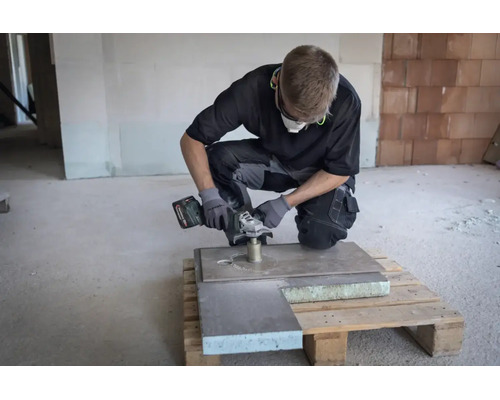 Handwerker bohrt mit einem Metabo Winkelschleifer und einer Diamantbohrkrone ein Loch in eine Steinplatte auf einer Baustelle.