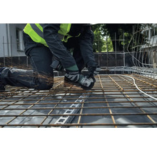 Ein Bauarbeiter trennt mit einem Metabo Akku-Winkelschleifer eine Bewehrungsmatte aus Stahl auf einer Baustelle.