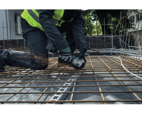 Ein Bauarbeiter trennt mit einem Metabo Akku-Winkelschleifer eine Bewehrungsmatte aus Stahl auf einer Baustelle.