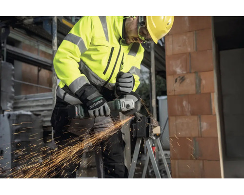 Handwerker mit Metabo Akku-Winkelschleifer trennt Metall auf einer Baustelle, Funkenflug, Schutzkleidung und Helm.