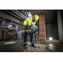 Bauarbeiter in Warnschutzkleidung und Schutzhelm nutzt einen Metabo Winkelschleifer an einem Werkstück auf einer Baustelle mit Funkenflug.