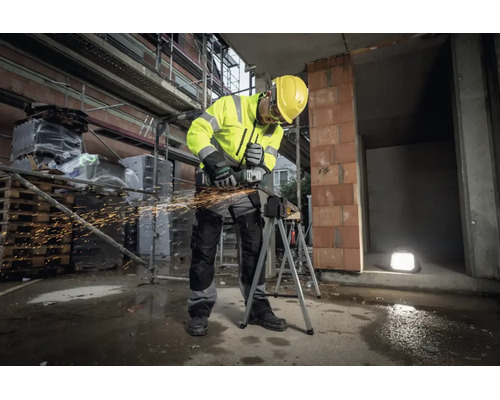 Bauarbeiter in Warnschutzkleidung und Schutzhelm nutzt einen Metabo Winkelschleifer an einem Werkstück auf einer Baustelle mit Funkenflug.