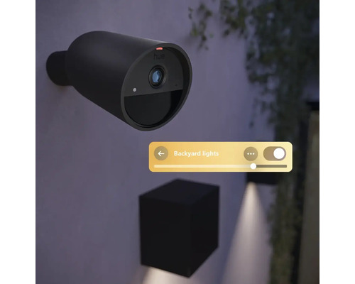 Caméra de surveillance Philips Hue Secure montée sur un mur extérieur, avec commande de l'éclairage de jardin via l'application.