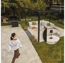 Salon de jardin moderne avec pergola noire, canapé d'angle, barbecue à gaz et une petite lampe de table noire sur une table basse.