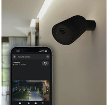 Caméra de sécurité Philips Hue pour l'extérieur, noire, fixée au mur avec vue en direct sur un smartphone.