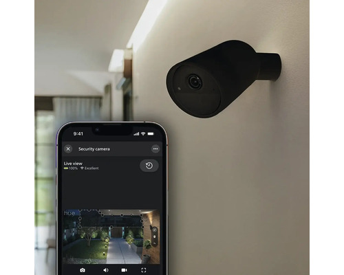 Caméra de sécurité Philips Hue pour l'extérieur, noire, fixée au mur avec vue en direct sur un smartphone.
