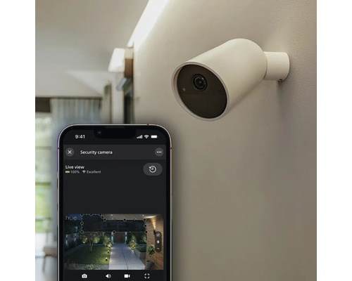 Caméra de surveillance Philips Hue Secure fixée au mur avec smartphone affichant l'image en direct dans l'application Hue.