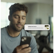 Homme regardant un smartphone avec une notification Philips Hue Secure indiquant un mouvement détecté par la caméra du jardin.