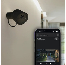 Caméra de sécurité Philips Hue Secure fixée au mur et smartphone avec application pour une vue en direct de l'espace extérieur.