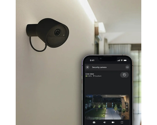 Caméra de sécurité Philips Hue Secure fixée au mur et smartphone avec application pour une vue en direct de l'espace extérieur.