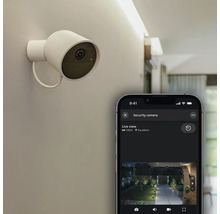 Caméra de sécurité intelligente blanche au mur avec application smartphone et flux vidéo en direct d'un jardin la nuit.