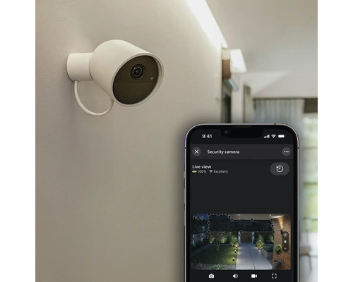 Caméra de sécurité intelligente blanche au mur avec application smartphone et flux vidéo en direct d'un jardin la nuit.