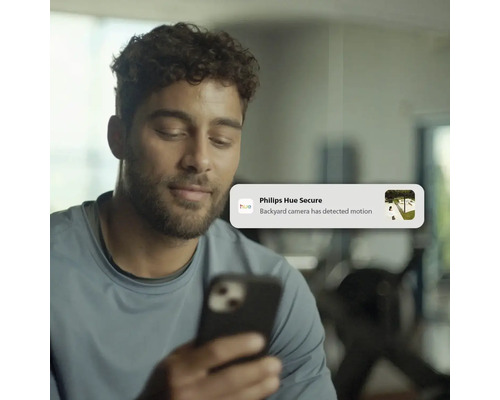 Homme regardant un smartphone avec une notification Philips Hue Secure indiquant un mouvement détecté par la caméra du jardin.