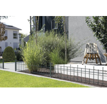 Niedriger Metallzaun in Anthrazit begrenzt ein Beet mit Ziergräsern neben einem Holzstuhl auf einer Terrasse im modernen Garten.