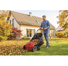 Un homme pousse un ramasseur de feuilles et d herbe rouge sur une pelouse parsemée de feuilles d automne devant une maison dans un cadre lumineux.