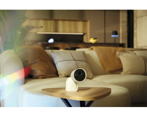 Caméra de surveillance blanche sur une table en bois dans un salon moderne avec canapé.
