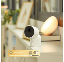 Caméra de surveillance intelligente blanche pour intérieur sur étagère, incluant le contrôle via une application de la lumière connectée.