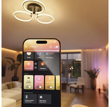 Application maison connectée sur un smartphone contrôlant un plafonnier LED moderne et l'éclairage d'ambiance dans un salon.