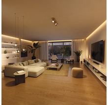 Salon moderne et spacieux avec canapé d'angle clair, table basse en bois, meuble TV et éclairage LED indirect sur un parquet chaleureux.