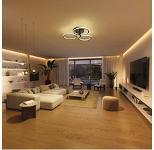 Salon moderne et lumineux avec plafonnier LED à trois anneaux, canapé, table basse et éclairage indirect.