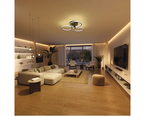 Salon moderne et lumineux avec plafonnier LED à trois anneaux, canapé, table basse et éclairage indirect.