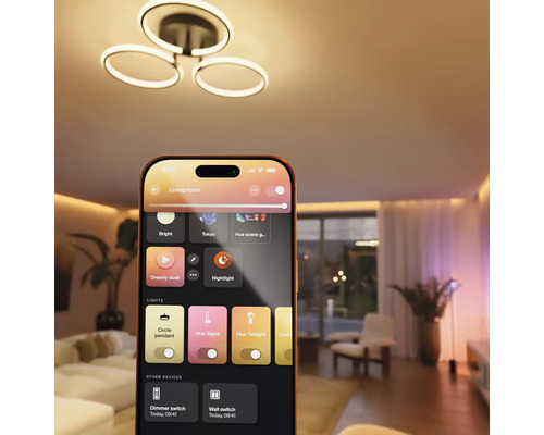 Application maison connectée sur un smartphone contrôlant un plafonnier LED moderne et l'éclairage d'ambiance dans un salon.