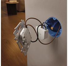 Module d interrupteur mural Philips Hue en cours d installation dans une boîte d encastrement et raccordé à un cadre d interrupteur.