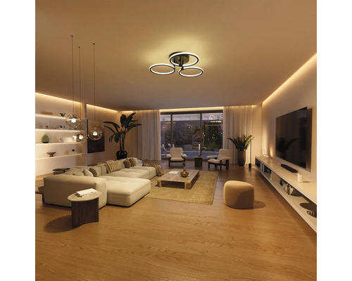 Salon moderne et lumineux avec plafonnier LED en forme d'anneaux, éclairage indirect et suspensions en verre.