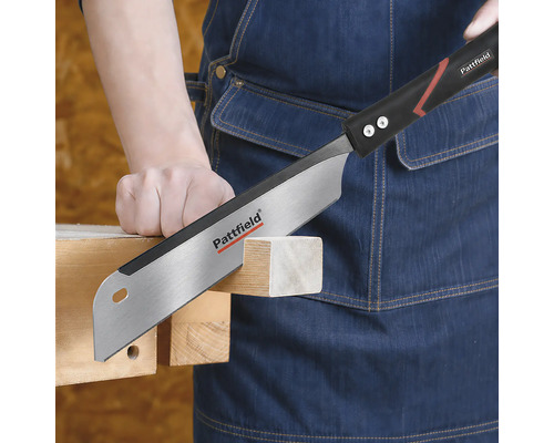 Scie à main Pattfield coupant une pièce de bois tenue par une personne portant un tablier en jean.