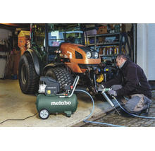 Compresseur Metabo Basic 250-50 lors de l'entretien d'un tracteur avec une pompe à graisse pneumatique dans un atelier organisé.