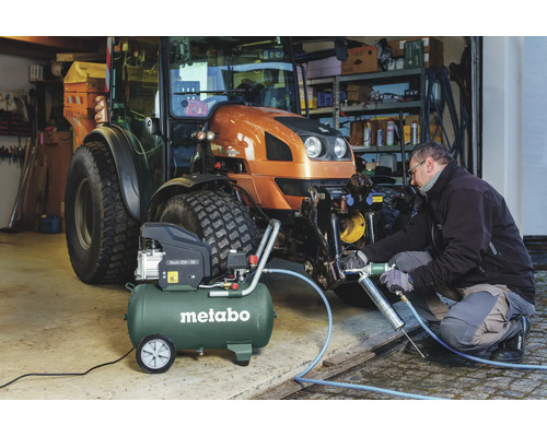 Compresseur Metabo Basic 250-50 lors de l'entretien d'un tracteur avec une pompe à graisse pneumatique dans un atelier organisé.