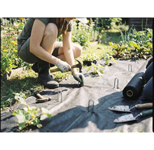 Une personne pose un feutre de jardinage et le fixe avec des piquets de fixation et un marteau.