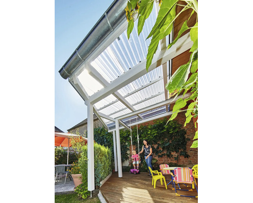 Terrassenüberdachung mit weißem Gestell und lichtdurchlässigen Wellplatten auf einer Holzterrasse in einem Garten mit Kletterpflanzen.