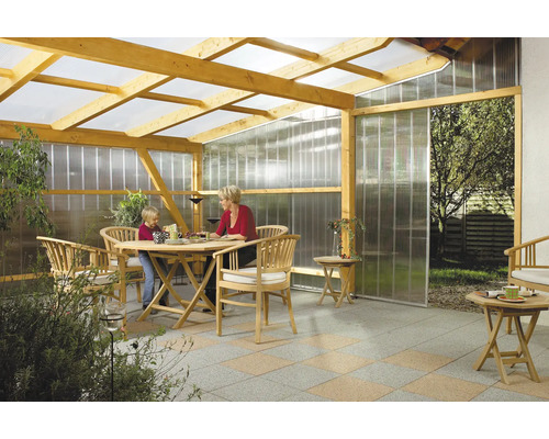 Toit de terrasse en bois avec plaques alvéolaires transparentes sur le toit et les parois, meublé de mobilier de jardin en bois sur dalles.