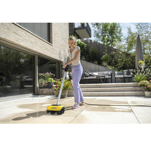 Eine Frau reinigt eine Steinterrasse mit einem elektrischen Kärcher Terrassenreiniger in einem modernen, hellen und organisierten Außenbereich.