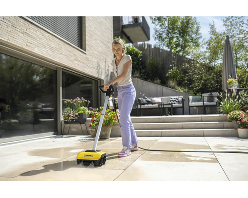 Eine Frau reinigt eine Steinterrasse mit einem elektrischen Kärcher Terrassenreiniger in einem modernen, hellen und organisierten Außenbereich.