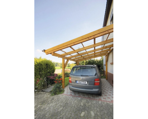Holz-Anlehncarport mit lichtdurchlässigen Wellplatten an einer Hauswand, darunter parkt ein Auto auf gepflastertem Boden.