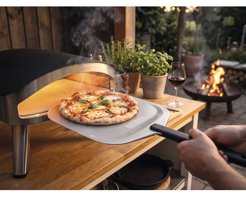 Pizza fraîchement cuite retirée d'un four à pizza portable sur une table en bois dans un jardin avec une pelle à pizza avec Tenneker Logo.