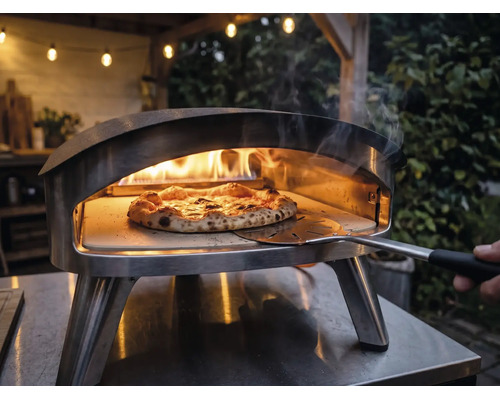 Four à pizza extérieur en acier inoxydable avec des flammes et une pizza sur pierre à pizza manipulée avec une pelle à pizza.