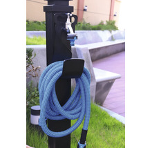 Fontaine de jardin noire avec robinet argenté et tuyau d'arrosage bleu enroulé sur un support à l'extérieur.