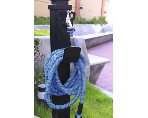 Fontaine de jardin noire avec robinet argenté et tuyau d'arrosage bleu enroulé sur un support à l'extérieur.