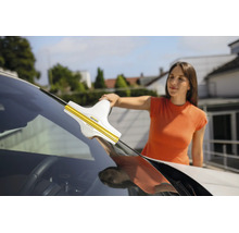 Une femme nettoie le pare-brise d'une voiture avec un nettoyeur de vitres Kärcher.