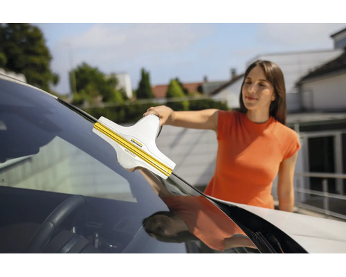 Une femme nettoie le pare-brise d'une voiture avec un nettoyeur de vitres Kärcher.