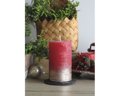 Strukturierte Stumpenkerze in Rot und Gold auf Schieferuntersetzer in weihnachtlicher Szene mit grünen Zweigen und rotem Spielzeug-Lastkraftwagen.