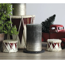 Zylindrische Stumpenkerze mit strukturierter Oberfläche in festlicher Weihnachtsszene mit Trommeln, einem roten Spielzeug-Lastwagen und kleinen Tannen.
