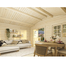 Vue intérieure d un abri de jardin en bois clair avec un coin salon, un canapé, une table à manger et vue sur le jardin.