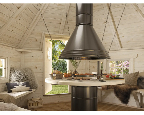 Innenansicht einer Grillkota aus Holz mit zentralem Grill, großer Dunstabzugshaube und Sitzbänken mit Kissen und Fellen.