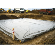 Grande bâche de protection grise posée sur le sol d'un chantier avec des engins de construction en arrière-plan.